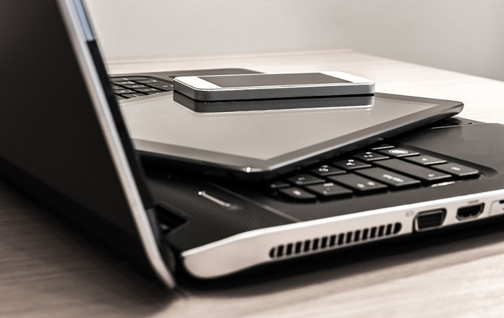 An image of a laptop with a cell phone and tablet on top of it.